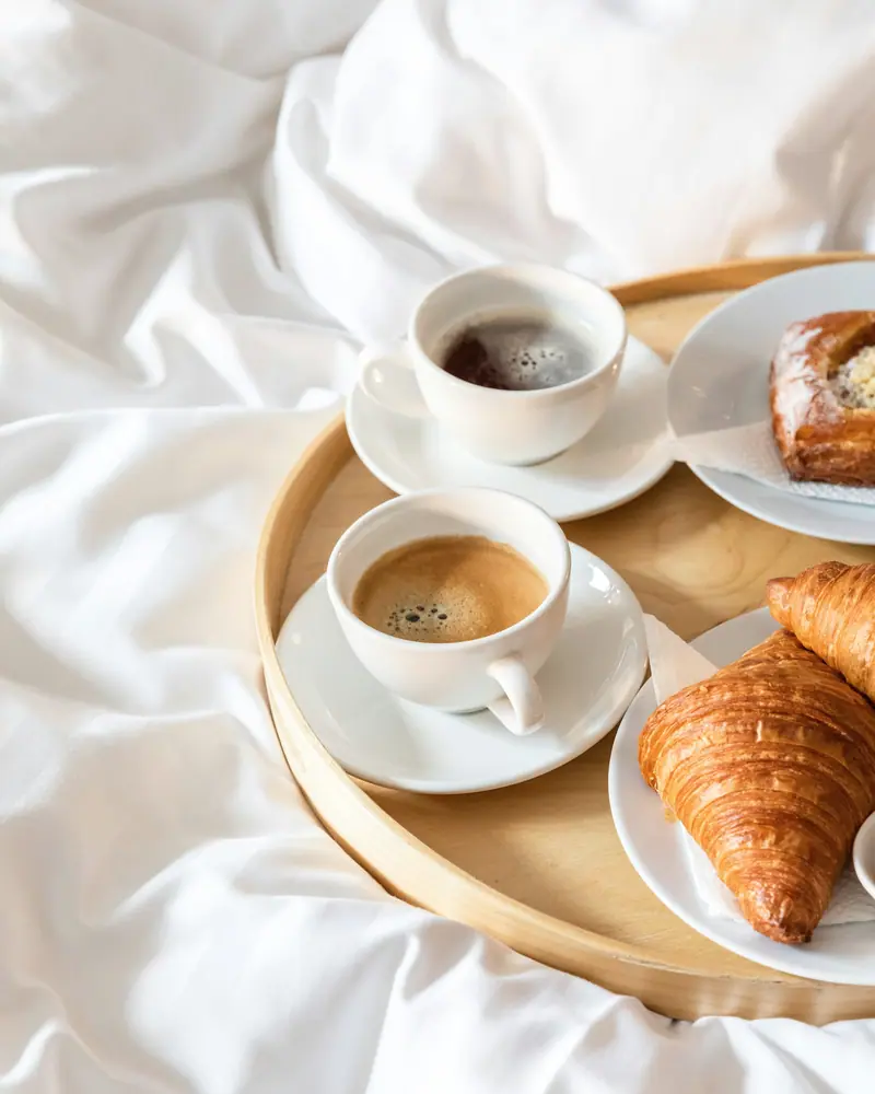 Plateau de petit-déjeuner sur des draps blancs : deux cafés et des croissants