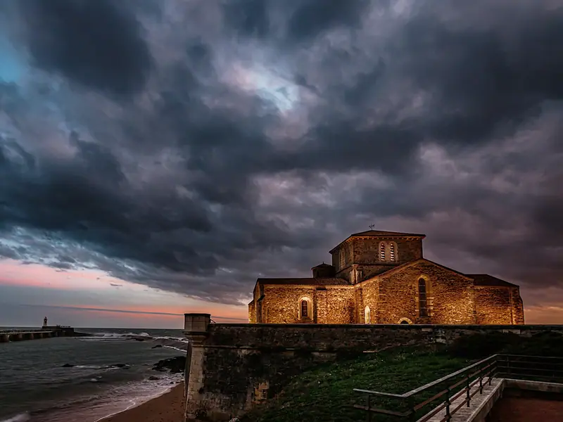 Une chapelle romane éclairée sous un ciel d’orage, au bord de l’eau