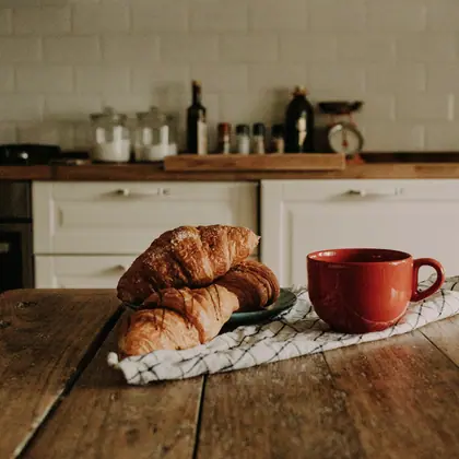 Deux croissants et une tasse rouge sur une table en bois