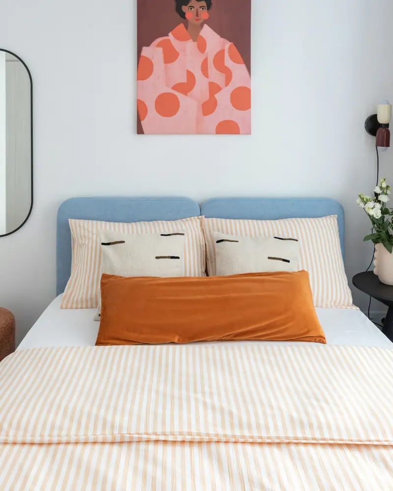 Lit double en linge rayé orange et tête de lit bleu clair, mur blanc